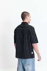 Camisa de manga corta con corte oversize, a rayas verticales blancas y grises, con cuello clásico y cierre frontal con botones. Confeccionada en algodón.