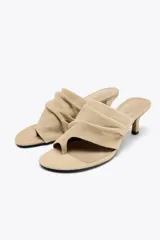 Sandalia color beige de ante, estilo mule, con tira ancha arrugada y posición para el dedo. Tacón fino medio y acabado en punta redonda.