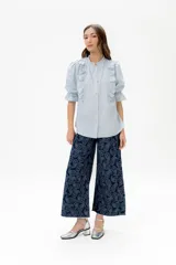 Blusa de lino color rojo con volados frontales que enmarcan el pecho, cuello redondo con mini volado y mangas 3/4 abullonadas con puño elástico. Presenta un cierre frontal con botones y una silueta relajada.