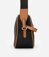 Cartera bandolera negra con detalles en marrón, confeccionada en poliéster certificado Grs y poliuretano. Presenta un aplique metálico triangular, asa larga ajustable y cierre por cremallera.