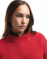 Sweater unisex de lana merino fina color rojo, con cuello redondo y corte relajado. Presenta un motivo inspirado en la técnica de zurcido visible.
