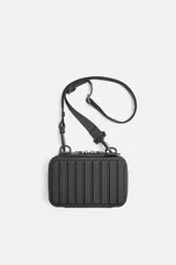 Bandolera rígida negra con acabado engomado y relieve. Tiene un compartimento principal con doble cremallera, un bolsillo interior de rejilla y asa de hombro ajustable y extraíble.