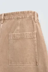 Pantalón de jean color beige, de corte ancho y tiro medio, con cinco bolsillos, efecto lavado y cierre frontal con cremallera y botón.