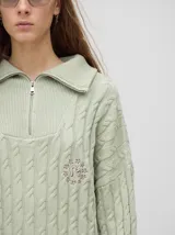 Sweater de punto color verde claro con cuello polo con cierre de cremallera, mangas largas y diseño con trenzas. Puños acanalados con rayas en color borgoña y blanco.