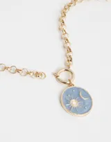 Collar corto dorado con cadena de eslabones gruesos y dije redondo esmaltado en color celeste con diseño de sol, luna y estrellas.