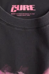 Remera negra de algodón con estampado del logo de la banda The Cure en tonos rosa y naranja. Corte oversized, cuello redondo y mangas cortas.