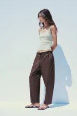 Pantalón marrón tipo barrel, de tiro medio con cintura elástica ajustable con lazada, bolsillos laterales y falsos bolsillos de vivo en la espalda.