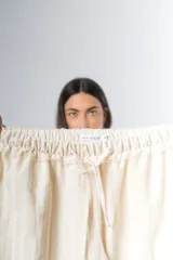 Pantalón de algodón color crudo con rayas verticales finas en beige, corte recto, cintura con elástico y detalle de puntilla en cintura y ruedo.