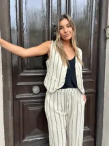 Conjunto de lino color crema con rayas verticales negras, compuesto por un chaleco con botones y un pantalón de corte recto con cintura elastizada y cordón ajustable.