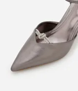 Zapato de tacón color gris con punta fina, tira fina con hebilla en el tobillo y detalle de nudo con strass.