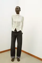 Jeans de tiro alto color negro lavado, con cintura cruzada, cinco bolsillos y pernera recta. El bajo está acabado en vuelta y tiene cierre frontal cruzado con cremallera y botones.