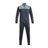 Conjunto deportivo Under Armour de hombre, compuesto por campera con cierre y pantalón largo. La campera es de color gris en la parte superior y azul marino en la parte inferior, con logo de la marca en el pecho. El pantalón es azul marino con logo de la marca en la pierna.