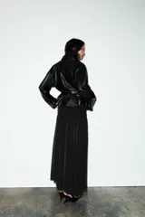 Cazadora negra de efecto piel, con cuello solapa y manga larga acabada en puño. Tiene bolsillos de vivo en delantero, cinturón lazada en mismo material y bajo acabado peplum. El cierre frontal es con cremallera.