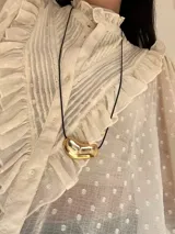 Collar con cadena fina negra y dije plateado con forma irregular.