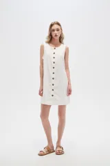 Vestido blanco de lino, corte entallado, con botones frontales, cuello a la base y breteles anchos.