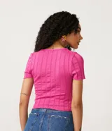 Blusa de punto color fucsia con cuello redondo y mangas cortas. Tiene una malla texturizada con material responsable en la composición.