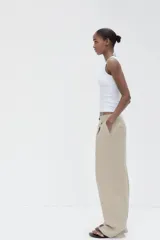 Pantalón color beige de tiro medio con trabillas, pliegues frontales y corte ancho.