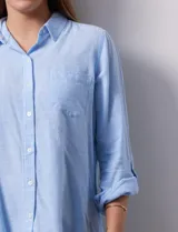 Camisa celeste de lino, con cuello con solapa, escote en V y abertura central con botones. Largo de manga regulable con presilla y botón. Delantera con bolsillo aplicado.