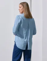 Camisa celeste de tencel con cuello con solapa, escote en V, abertura central con botones y mangas 3/4 regulables con presilla y botón.