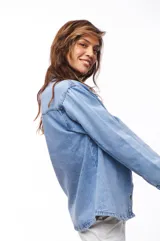 Sobrecamisa celeste de jean con cuello camisero, cierre frontal con botones dorados, dos bolsillos con solapa en el pecho y mangas largas con puños abotonados.