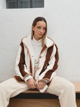 Campera con capucha, de tela tipo peluche a rayas verticales color marrón y blanco, con ribete color beige.