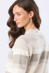 Buzo tejido de abrigo con rayas horizontales en tonos beige, blanco y gris. Tiene cuello redondo y mangas largas.