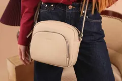 Bandolera de cuero sintético color beige, con diseño compacto y elegante. Cuenta con un bolsillo frontal con cierre y un compartimento principal con cierre. La correa es regulable.