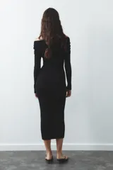 Vestido largo de punto negro con escote recto, hombros descubiertos, mangas largas y detalle de pieza metálica en el delantero.