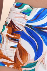 Calzón de bikini tiro alto con frunces laterales y estampado botánico en tonos azules, marrones y verdes sobre fondo blanco.