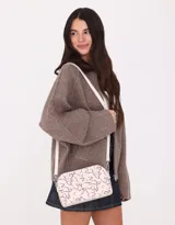 Bandolera negra de cuerina con doble compartimento con cierre y charm lateral. Tiene correa regulable y desmontable.