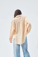 Camisa color durazno confeccionada en algodón, de corte amplio, con cuello solapa, manga larga con puños abotonados, hombros caídos, bolsillo de parche en el pecho, pinzas en la espalda y cierre frontal con botones.