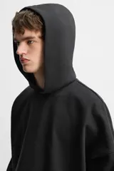 Sudadera con capucha negra, de corte oversize, confeccionada en tejido de algodón con interior en rizo. Cuenta con manga larga, bolsillos frontales tipo canguro, efecto lavado y acabados irregulares con vuelta.