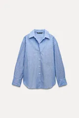 Camisa celeste con rayas verticales blancas, de corte holgado, cuello solapa, escote en pico y mangas largas con puños abotonados.