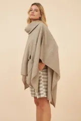 Poncho de lana color marrón con cuello alto, mangas 3/4 y bolsillo lateral con detalle de botones de cuero.