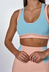 Conjunto deportivo de calza corta y top color salmón con detalles en celeste. El top es de corte deportivo con breteles anchos y el logo 'bk' estampado en el frente. La calza es de tiro alto y corte ajustado.
