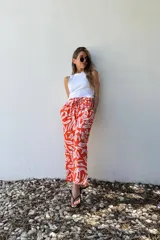 Pantalón de corte amplio, color naranja con estampado abstracto en blanco, cintura elastizada y bolsillos laterales.