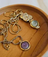 Collar con cadena de eslabones dorados y dije redondo con piedra amatista engarzada en metal dorado.