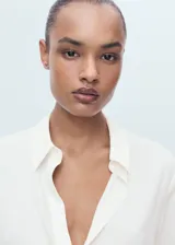 Camisa blanca de manga larga con puños abotonados, cuello camisero y cierre frontal de botones. Diseño recto con tejido fluido.