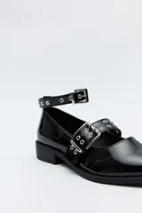 Zapato tipo zueco negro charol con punta fina, doble tira con hebillas metálicas y pulsera al tobillo con tachas.