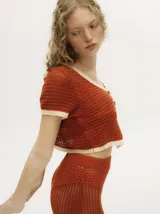 Top tejido calado color azul petróleo con cuello en V y botones carey. Tiene mangas cortas y puños en color amarillo contrastante.