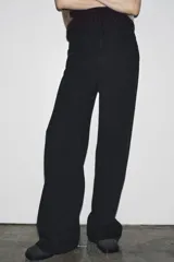 Pantalón de jean negro de corte palazzo, tiro medio y cintura con trabillas. Tiene bolsillos delanteros y traseros, raya planchada en el frente y cierre frontal con cremallera, botón y ganchos metálicos.