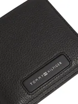 Billetera de cuero granulado negro, con diseño plegable y logo de Tommy Hilfiger en la parte inferior.