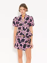 Top con estampado de flores rosas y verdes sobre fondo azul marino, cuello mao con jareta y tiras de gamuza para anudar. Escote en forma de gota, acceso mediante botones forrados en tela base, corte en cintura que le da vuelo a la cadera y mangas abullonadas con elástico en el puño.