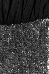 Vestido corto con parte superior negra de manga larga y escote barco drapeado, y falda corta de lentejuelas plateadas.