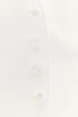 Top chaleco blanco de tejido satinado con cuello halter ajustable con hebilla metálica, falsos bolsillos de doble vivo en delantero, espalda descubierta con tira ajustable y cierre frontal con botones.