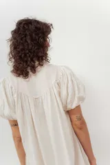 Vestido color beige con botones frontales, cuello camisero, mangas cortas abullonadas y falda con volantes.