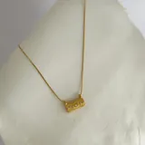 Collar dorado con cadena de eslabones y dije rectangular con textura y cristales incrustados.