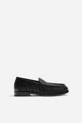 Mocasín de cuero negro con diseño trenzado en la parte superior, horma redonda y suela con ligero tacón.