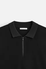 Polo negro de punto con cuello solapa y cierre frontal de cremallera.