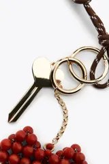 Llavero con cordón marrón y blanco, llave dorada y dije colgante de corazón rojo hecho con cuentas. Incluye aros metálicos dorados.